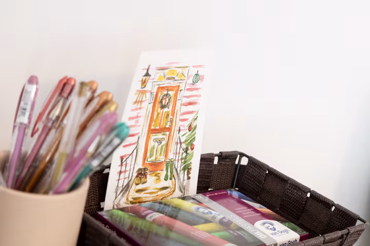 Bolígrafos de colores, dibujo de una puerta y cesta con materiales de pintura
