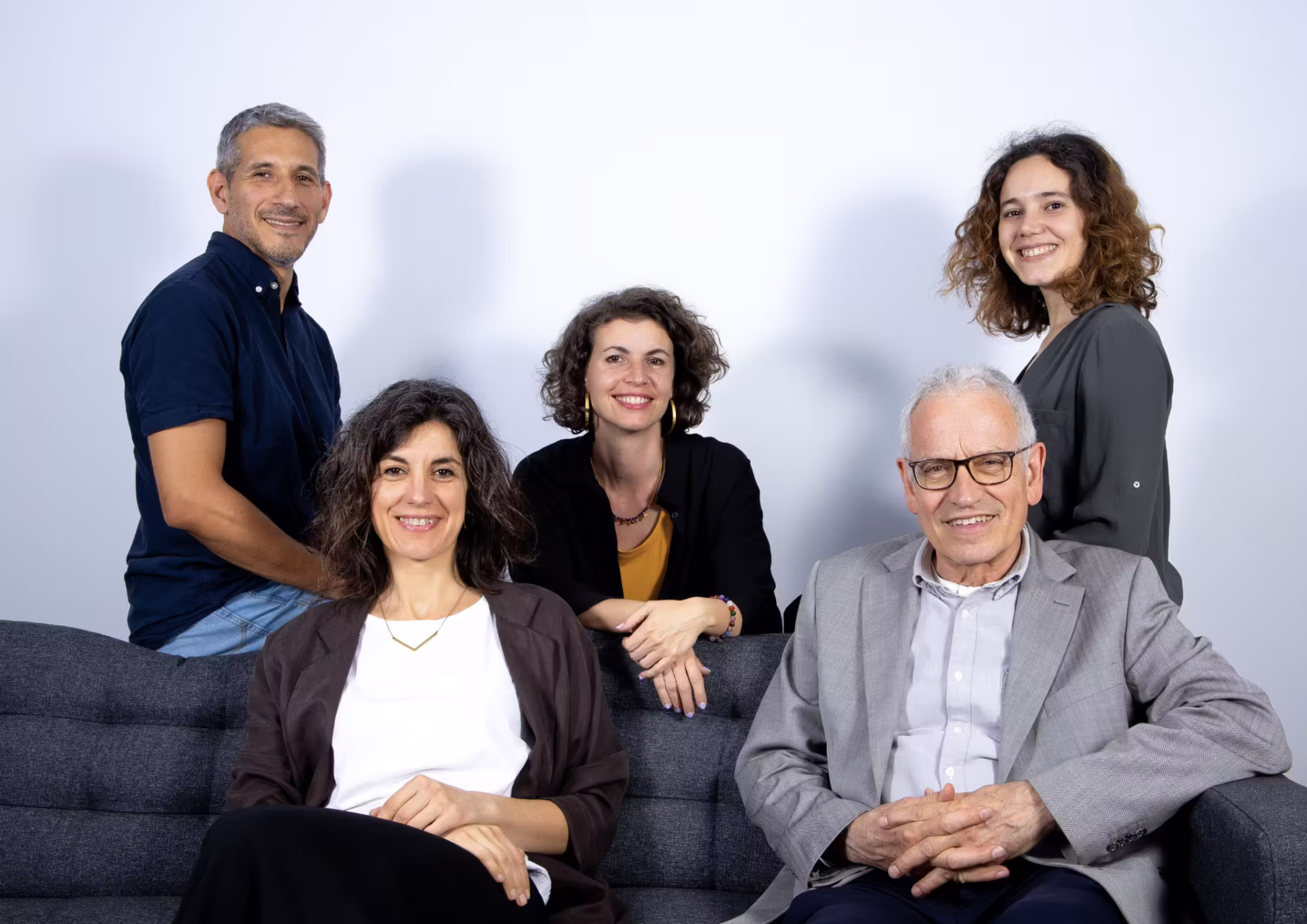 Equipo de Clínica Synaptica sonriendo en torno a un sofá gris