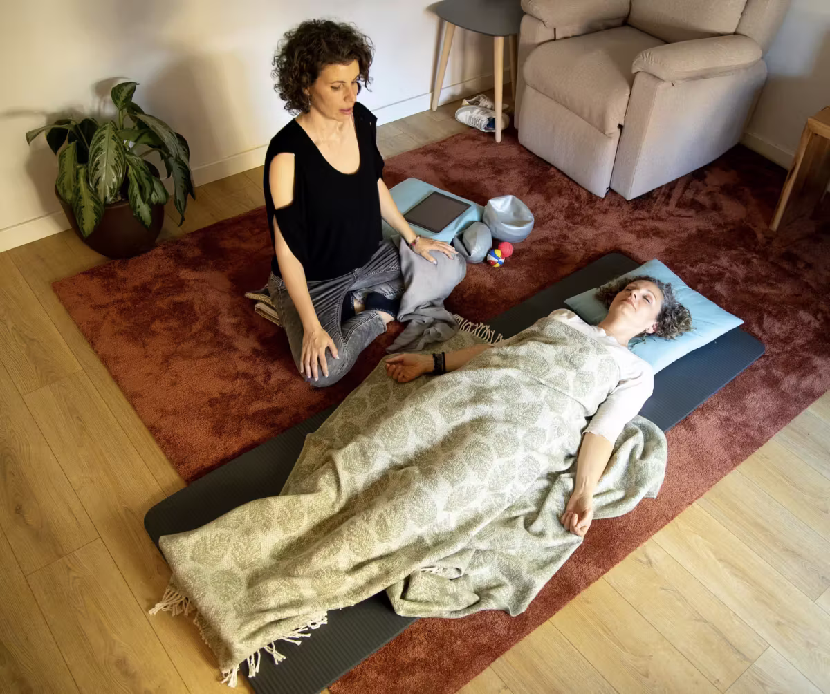 Terapeuta acompaña a una mujer tumbada con manta en una sesión de TRE