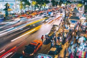 Calle concurrida de noche con tráfico en movimiento y puestos callejeros