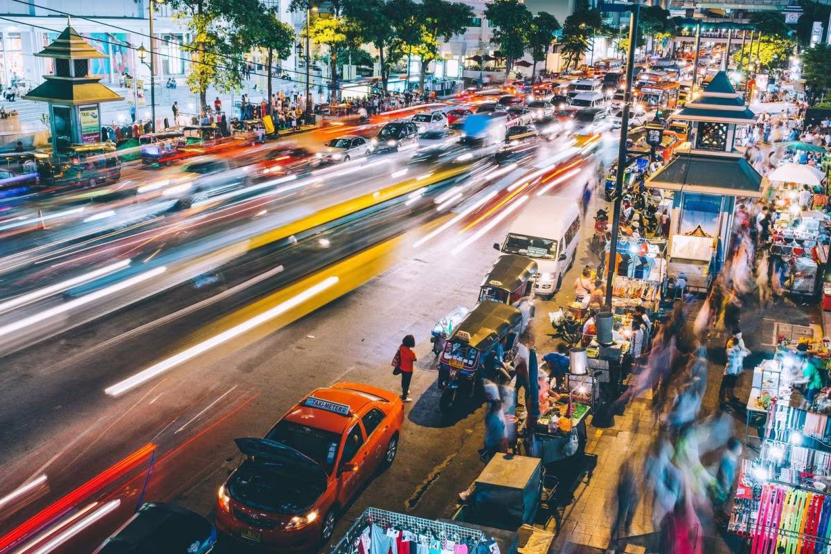 Calle concurrida de noche con tráfico en movimiento y puestos callejeros