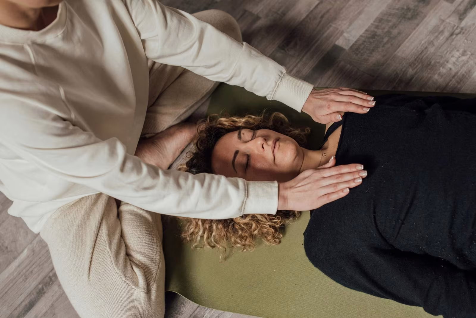 Terapeuta con las manos junto a la cabeza de una mujer tumbada en esterilla
