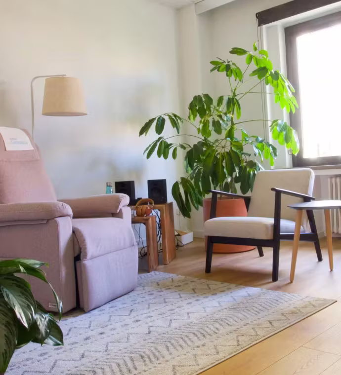 Sala de terapia con sillón reclinable rosa, butaca, plantas y altavoces