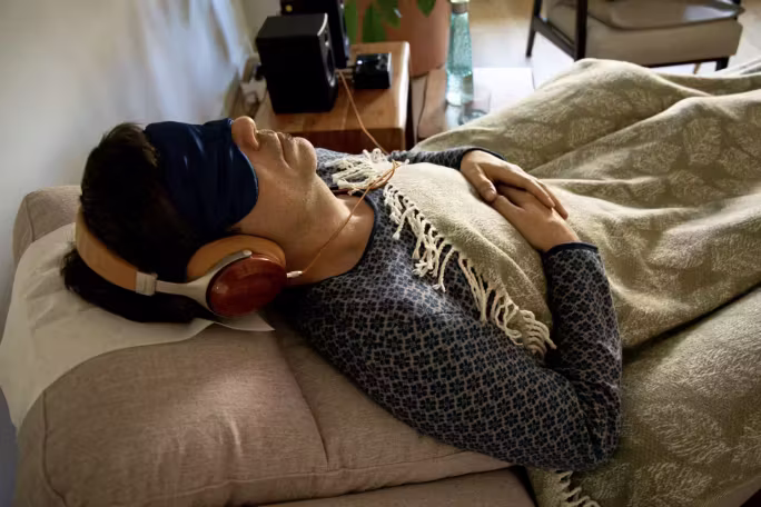 Hombre tumbado en un sofá con antifaz, auriculares y una manta