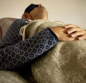 Hombre recostado con antifaz y las manos sobre una manta
